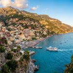 Panoramic view of pastel cliffside village of Positano on the Amalfi Coast with a white public passenger ferry cruising into the turquoise Mediterranean bay