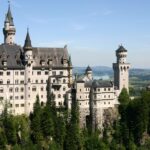 Panoramic view of Neuschwanstein Castle perched above Bavarian alpine foothills and Lake Forggensee