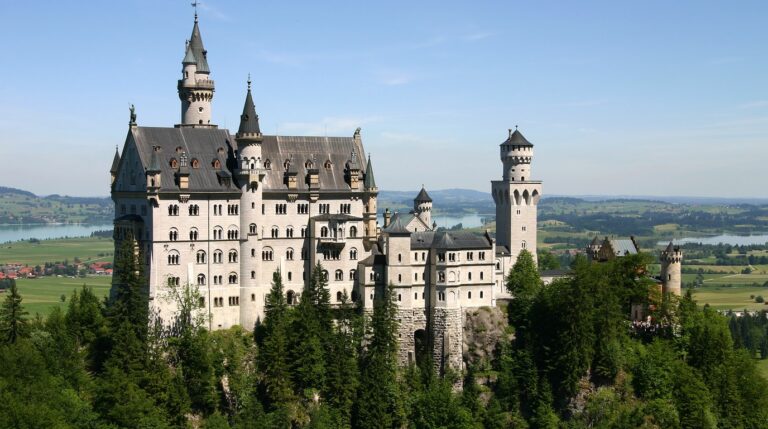 Panoramic view of Neuschwanstein Castle perched above Bavarian alpine foothills and Lake Forggensee