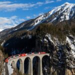A classic red Swiss mountain train crossing the majestic curved stone arches of Landwasser Viaduct in the Grisons Alps