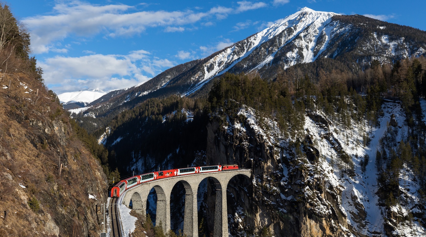 A classic red Swiss mountain train crossing the majestic curved stone arches of Landwasser Viaduct in the Grisons Alps