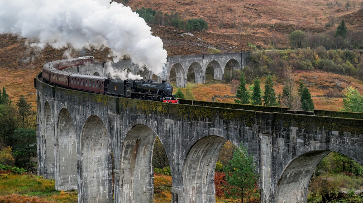 Panoramic view of a train crossing the iconic curving concrete arches of Glenfinnan Viaduct surrounded by Scottish Highland hills