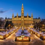 Illuminated Vienna Christmas Market on Rathausplatz at twilight with glowing market chalets and decorated Christmas tree in front of the neo-Gothic City Hall