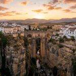 Spectacular wide-angle panoramic sunset view of the monumental Puente Nuevo bridge spanning El Tajo gorge in Ronda Spain with whitewashed houses on cliff edge