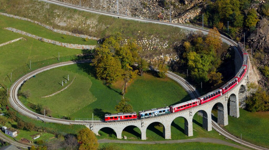 A classic red RhB Swiss regional train gracefully negotiating the sweeping circular arches of the Brusio Spiral Viaduct