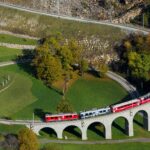 A classic red RhB Swiss regional train gracefully negotiating the sweeping circular arches of the Brusio Spiral Viaduct