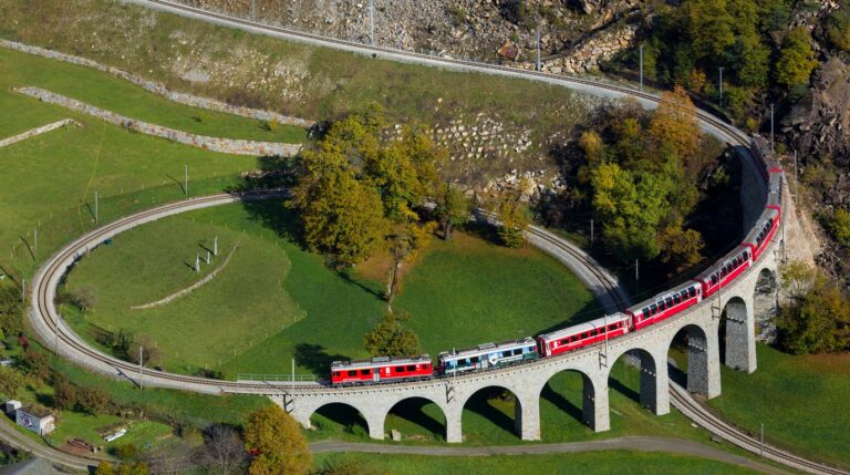A classic red RhB Swiss regional train gracefully negotiating the sweeping circular arches of the Brusio Spiral Viaduct