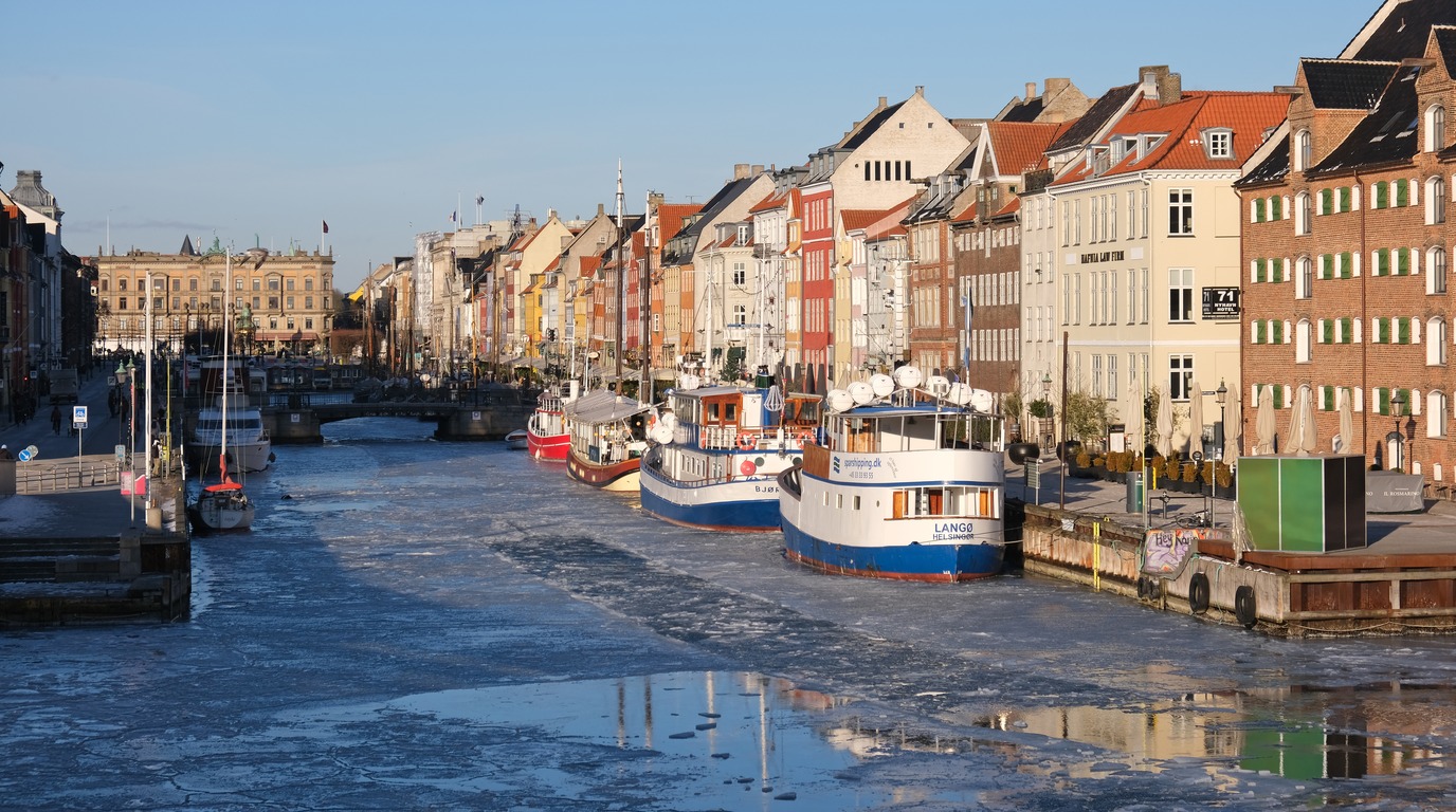 Snow dusted colorful 17th century townhouses and historic wooden ships along Nyhavn canal in winter Copenhagen Denmark