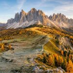 Breathtaking wide-angle panoramic view of the Seceda ridgeline and Odle Geisler mountain peaks in the Italian Dolomites during peak autumn with golden larch forests