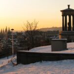 Panoramic winter sunset view from Calton Hill over the historic spires and Edinburgh Castle in Scotland with Dugald Stewart Monument in the foreground