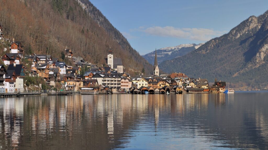 Panoramic postcard view of Hallstatt village, historic church steeple, and alpine reflections across Lake Hallstatt in Upper Austria