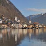 Panoramic postcard view of Hallstatt village, historic church steeple, and alpine reflections across Lake Hallstatt in Upper Austria