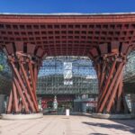 The monumental wooden Tsuzumi-mon drum gate illuminated at twilight in front of Kanazawa Station