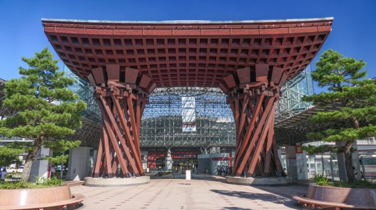 The monumental wooden Tsuzumi-mon drum gate illuminated at twilight in front of Kanazawa Station