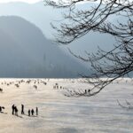 Frozen Lake Bled in winter with the pilgrimage church on the island reflected in icy water and snow-capped peaks of the Julian Alps Slovenia