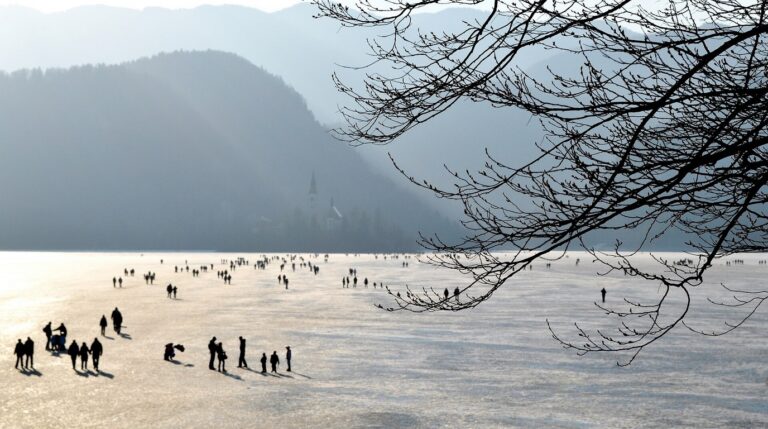 Frozen Lake Bled in winter with the pilgrimage church on the island reflected in icy water and snow-capped peaks of the Julian Alps Slovenia