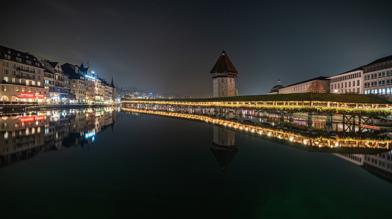 Historic wooden Chapel Bridge Kapellbrucke and octagonal Water Tower in Lucerne Switzerland with snowy mountains
