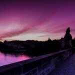 Panoramic winter view of Charles Bridge at pink sunrise over the misty Vltava river with Prague Castle in Czech Republic