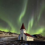 Vibrant green Aurora Borealis Northern Lights dancing across the starry night sky over snowy winter landscape and church near Reykjavik Iceland