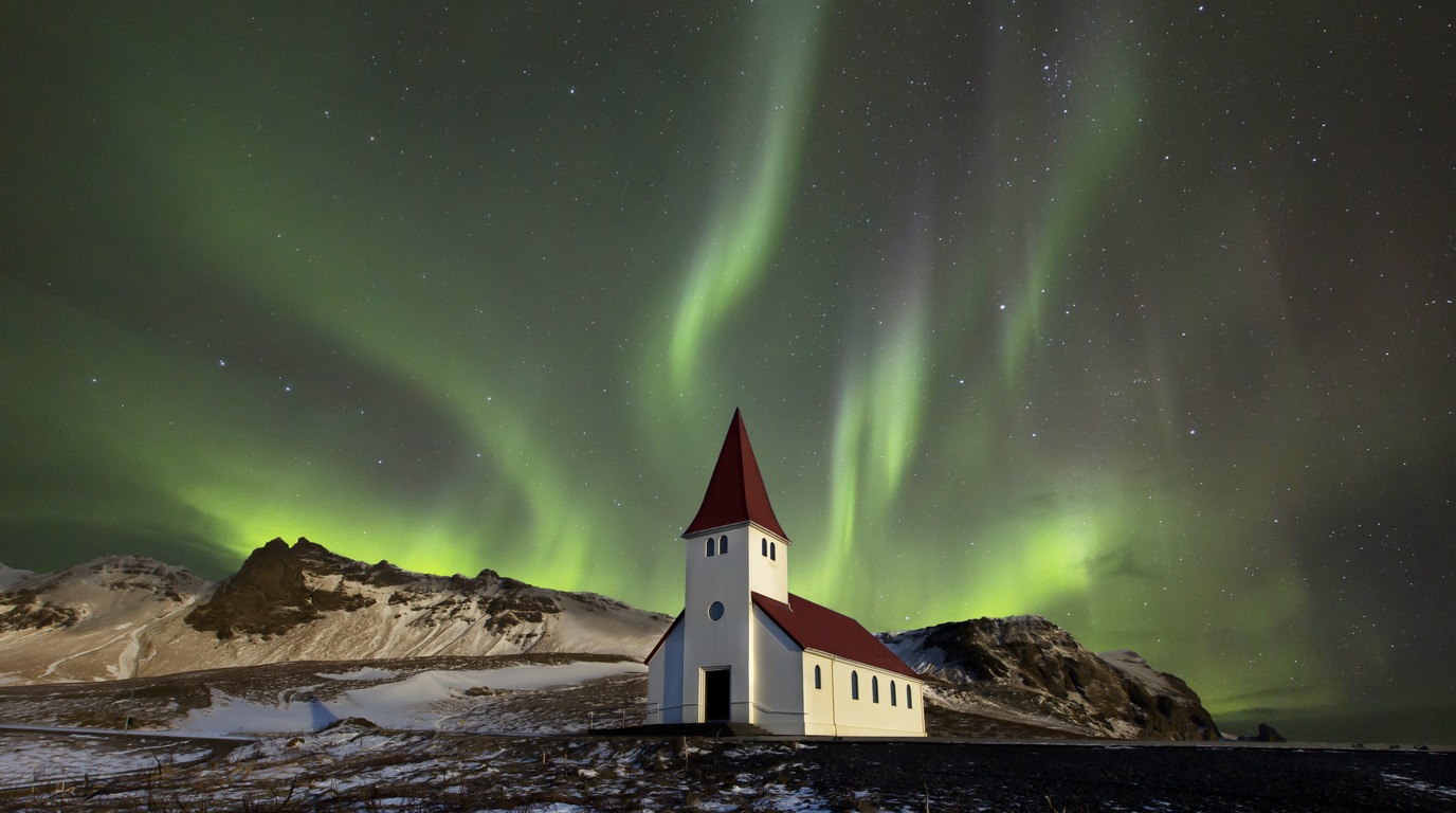 Vibrant green Aurora Borealis Northern Lights dancing across the starry night sky over snowy winter landscape and church near Reykjavik Iceland