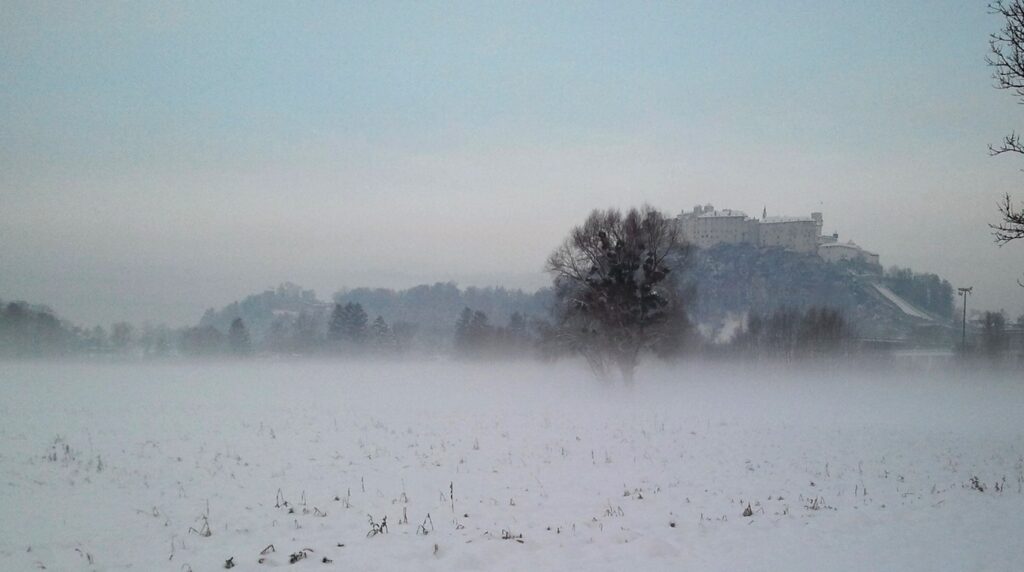 Panoramic winter view of Hohensalzburg Fortress high on a snowy cliff above Baroque church domes and historic rooftops of Salzburg Austria