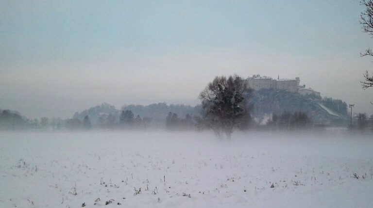 Panoramic winter view of Hohensalzburg Fortress high on a snowy cliff above Baroque church domes and historic rooftops of Salzburg Austria