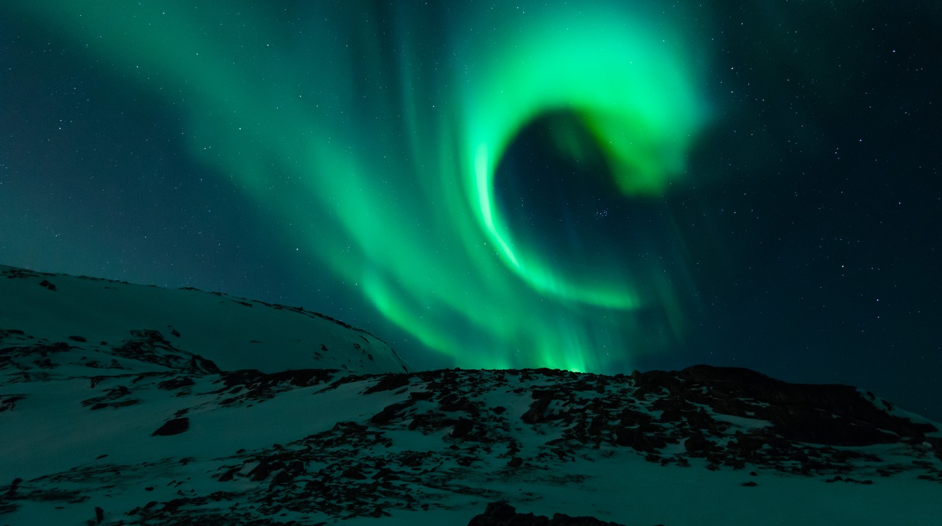 Vibrant green Aurora Borealis Northern Lights dancing across the dark Arctic sky over snowy mountains in Tromsø Norway