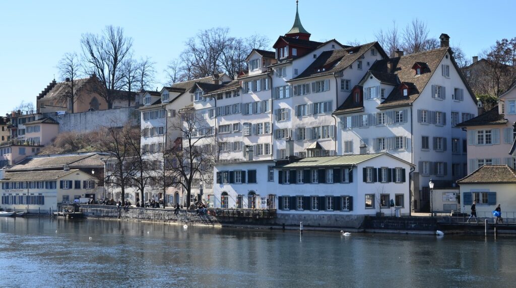 Panoramic view of the historic Grossmunster cathedral towers and snow-covered rooftops of Zurich along the Limmat river in winter