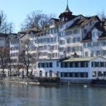 Panoramic view of the historic Grossmunster cathedral towers and snow-covered rooftops of Zurich along the Limmat river in winter