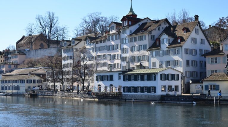 Panoramic view of the historic Grossmunster cathedral towers and snow-covered rooftops of Zurich along the Limmat river in winter
