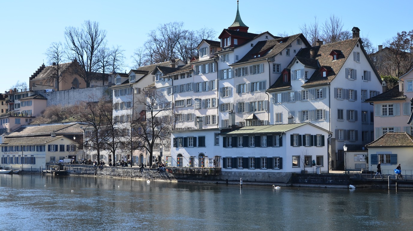 Panoramic view of the historic Grossmunster cathedral towers and snow-covered rooftops of Zurich along the Limmat river in winter